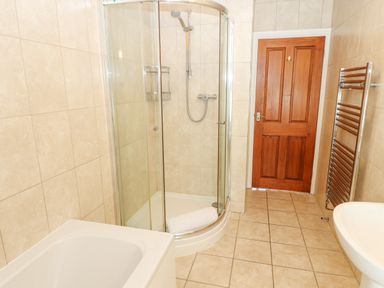 A bathroom with a bathtub shower with glass doors wooden door towel rail and sink at Goswick Hall in Bowland Bridge