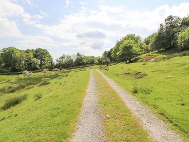 A gravel path running through a green grassy field with trees on both sides at Goswick Hall in Bowland Bridge