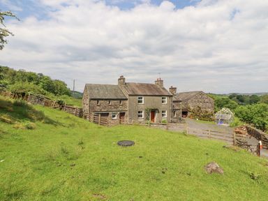 A stone farmhouse with adjacent buildings and green fields at Goswick Hall in Bowland Bridge