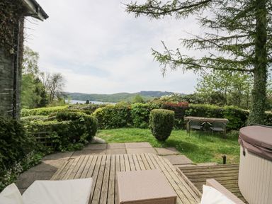 An outdoor patio area with chairs table and hot tub overlooking garden shrubs and distant hills at Lake Lodge in Bowness-On-Windermere