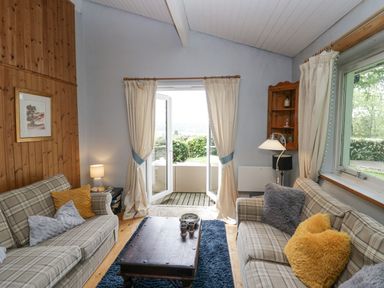 A sitting room with two sofas and a wooden coffee table in front of open patio doors at Lake Lodge in Bowness-On-Windermere