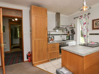 A kitchen with wooden cabinets a stove microwave and a window with floral curtains at Lake Lodge in Bowness-On-Windermere