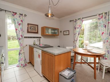 A kitchen with wooden cabinets a countertop a dishwasher a round wooden table two chairs and windows with floral curtains at Lake Lodge in Bowness-On-Windermere