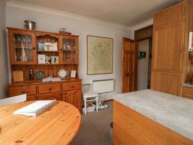 A kitchen with a wooden dining table and cupboard with glass doors a chair a wall-mounted heater and a map on the wall at Lake Lodge in Bowness-On-Windermere
