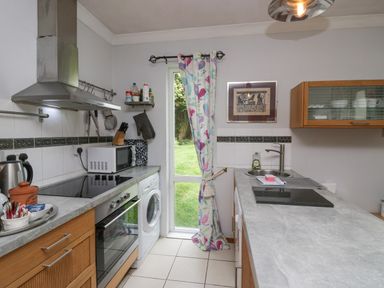 A kitchen with a stove washing machine microwave and a sink with a window and floral curtain at Lake Lodge in Bowness-On-Windermere