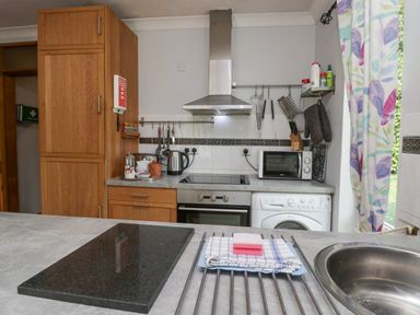 A kitchen with wooden cabinets a stove oven microwave kettle washing machine and a window with floral curtains at Lake Lodge in Bowness-On-Windermere