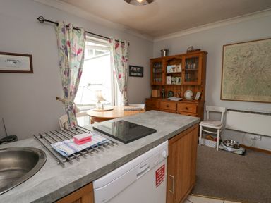 A kitchen area with a round table and chairs near a window with floral curtains a wooden cabinet with glass doors and a large map on the wall at Lake Lodge in Bowness-On-Windermere