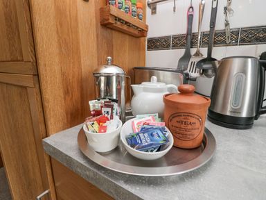 A kitchen counter with a teapot a kettle a French press a toaster a jar labeled tea and bowls with tea bags and coffee sachets at Lake Lodge in Bowness-On-Windermere