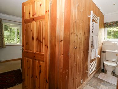 A bathroom with a wooden wall, white toilet, towel radiator with towels, and a small window with a floral curtain at Lake Lodge in Bowness-On-Windermere