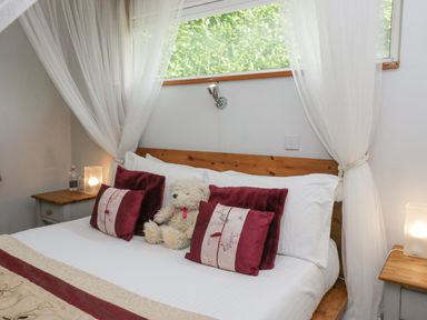 A bedroom with a wooden bed frame white bedding decorative pillows a teddy bear and bedside tables with lamps at Lake Lodge in Bowness-On-Windermere