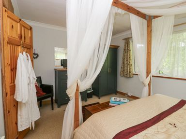 A bedroom with a four poster bed with white curtains a wooden chest two green wardrobes a black chair and robes hanging on a wooden door at Lake Lodge in Bowness-On-Windermere