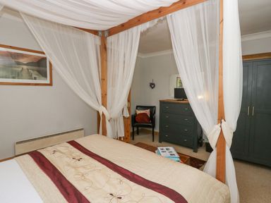 A bedroom with a four-poster bed with white curtains a dark dresser a black chair and a wardrobe at Lake Lodge in Bowness-On-Windermere