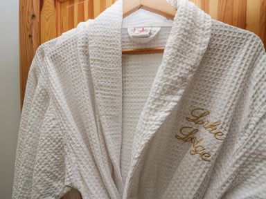 A white waffle-texture bathrobe with Lake Lodge embroidered hanging on a wooden door