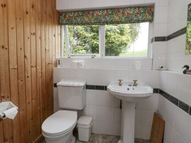 A bathroom with a toilet sink window with a floral curtain and wood paneling at Lake Lodge in Bowness-On-Windermere