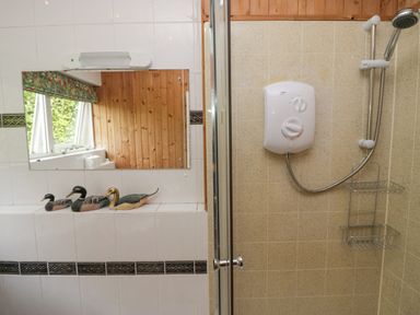A bathroom with a shower unit and a mirror above white tiled walls with three duck figurines on a ledge at Lake Lodge Bowness-On-Windermere