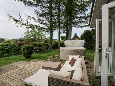 A garden with a cushioned outdoor sofa hot tub and wooden dining table at Lake Lodge in Bowness-On-Windermere