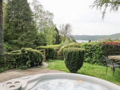 A garden with a hot tub bushes outdoor table and chairs and a lake view at Lake Lodge in Bowness-On-Windermere