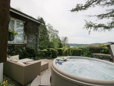 An outdoor patio with a hot tub seating area and garden furniture overlooking greenery and distant hills at Lake Lodge in Bowness-On-Windermere