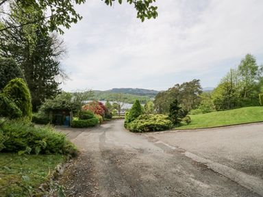 A garden path with shrubs trees and a distant view of a lake and hills at Lake Lodge in Bowness-On-Windermere