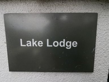 A black sign with white text reading Lake Lodge on a white textured wall at Lake Lodge in Bowness-On-Windermere