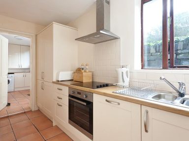A kitchen with white cabinets a stove oven sink and a window at Honeysuckle Cottage in Bowness