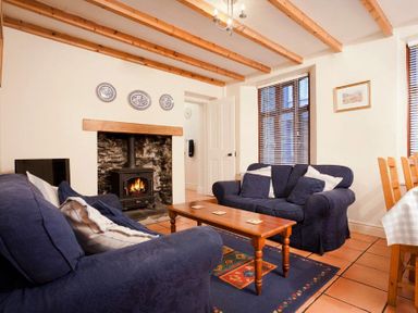 A living room with two blue sofas a wooden coffee table a fireplace and wooden beams at Honeysuckle Cottage in Bowness