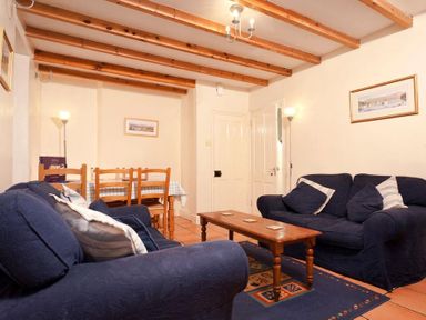 A living room with two blue sofas a wooden coffee table a dining table with chairs and exposed wooden beams on the ceiling at Honeysuckle Cottage in Bowness
