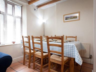 A dining area with a wooden table covered by a blue checkered tablecloth and six wooden chairs at Honeysuckle Cottage in Bowness