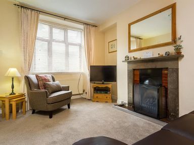 A living room with a plaid armchair lamp television and fireplace at Honeysuckle Cottage in Bowness