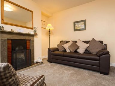 A living room with a leather sofa cushions fireplace and a standing lamp at Honeysuckle Cottage in Bowness