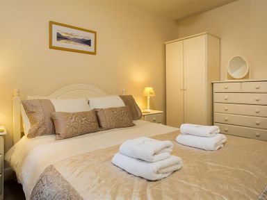 A bedroom with a bed with pillows towels bedside tables dresser wardrobe and a framed picture at Honeysuckle Cottage in Bowness