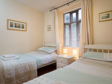 A bedroom with two twin beds a nightstand between them and framed pictures on the walls at Honeysuckle Cottage in Bowness