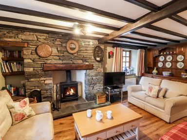 A living room with a stone fireplace wooden beams and two beige sofas at Gunpowder Cottage in Langdale
