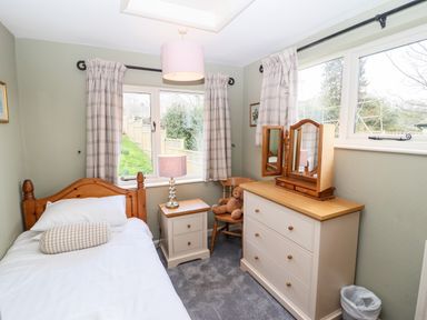 A small bedroom with a single bed side table and lamp chair teddy bear and chest of drawers at Gunpowder Cottage in Langdale