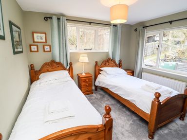 A bedroom with two single wooden beds white bedding bedside tables and two windows at Gunpowder Cottage in Langdale