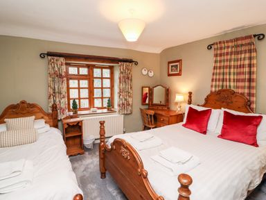 A bedroom with two wooden beds white bedding red pillows wooden dresser and window with floral curtains at Gunpowder Cottage in Langdale