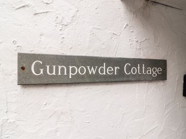 A metal sign with the text Gunpowder Cottage mounted on a white textured wall at Gunpowder Cottage in Langdale