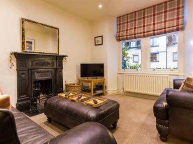 A living room with leather sofas a black fireplace a TV on a wooden stand and plaid window blinds at Orrest Range in Windermere