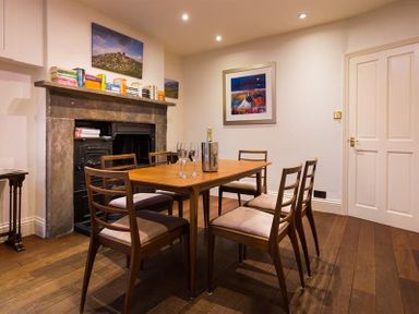 A dining room with a wooden table and six chairs and a fireplace with books on the mantelpiece at Orrest Range in Windermere