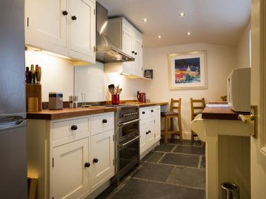 A kitchen with white cabinets a stove a microwave two wooden chairs and a framed painting on the wall at Orrest Range in Windermere