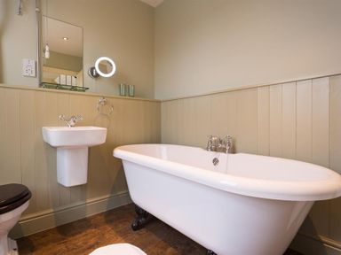 A bathroom with a freestanding bathtub, a wall-mounted sink, a toilet, and a mirror at Orrest Range in Windermere