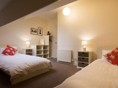 A bedroom with two single beds with red floral pillows two bedside tables with lamps and open shelving at Orrest Range in Windermere