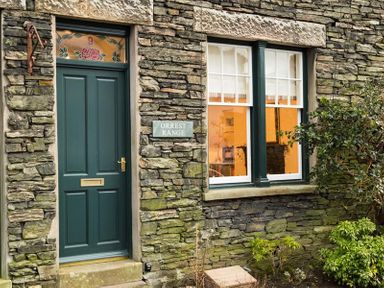 A green door and window set in a stone wall with plants outside at Orrest Range in Windermere