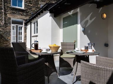 An outdoor patio area with two glass tables two wicker chairs a bowl with bananas and coffee items at Orrest Range in Windermere