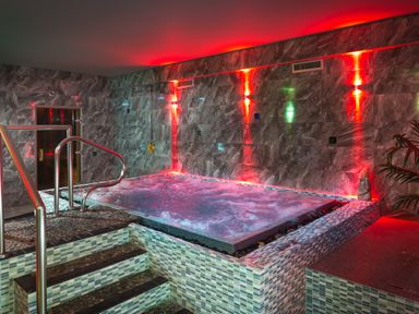 An indoor hot tub with steps and railings in a tiled room with red lighting at Orrest Range in Windermere