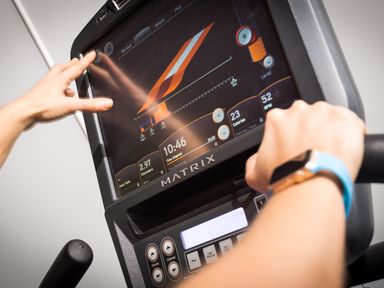 A close-up of a person using a touchscreen interface on a Matrix exercise bike at Orrest Range in Windermere