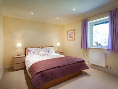 A bedroom with a double bed two bedside tables with lamps a window with purple curtains and a radiator at The Old Barn in Ambleside