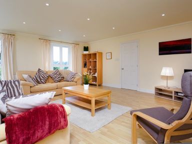 A living room with beige sofas, striped cushions, a wooden coffee table, a bookshelf, and a chair at The Old Barn in Ambleside