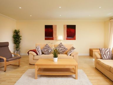 A living room with beige sofas, zebra print cushions, a wooden coffee table, a lamp, and a potted plant at The Old Barn in Ambleside