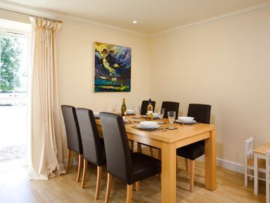 Dining room with wooden table and six chairs near window and abstract painting on wall at The Old Barn in Ambleside